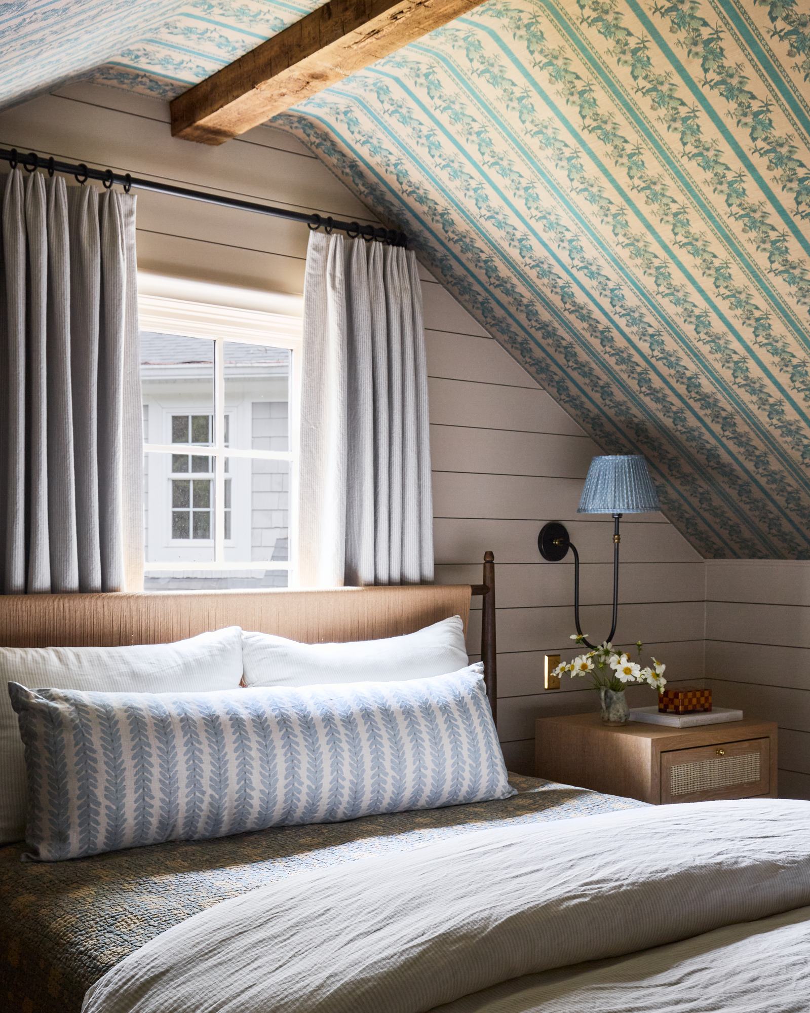 Attic primary bedroom with teal striped wallpaper and exposed beam