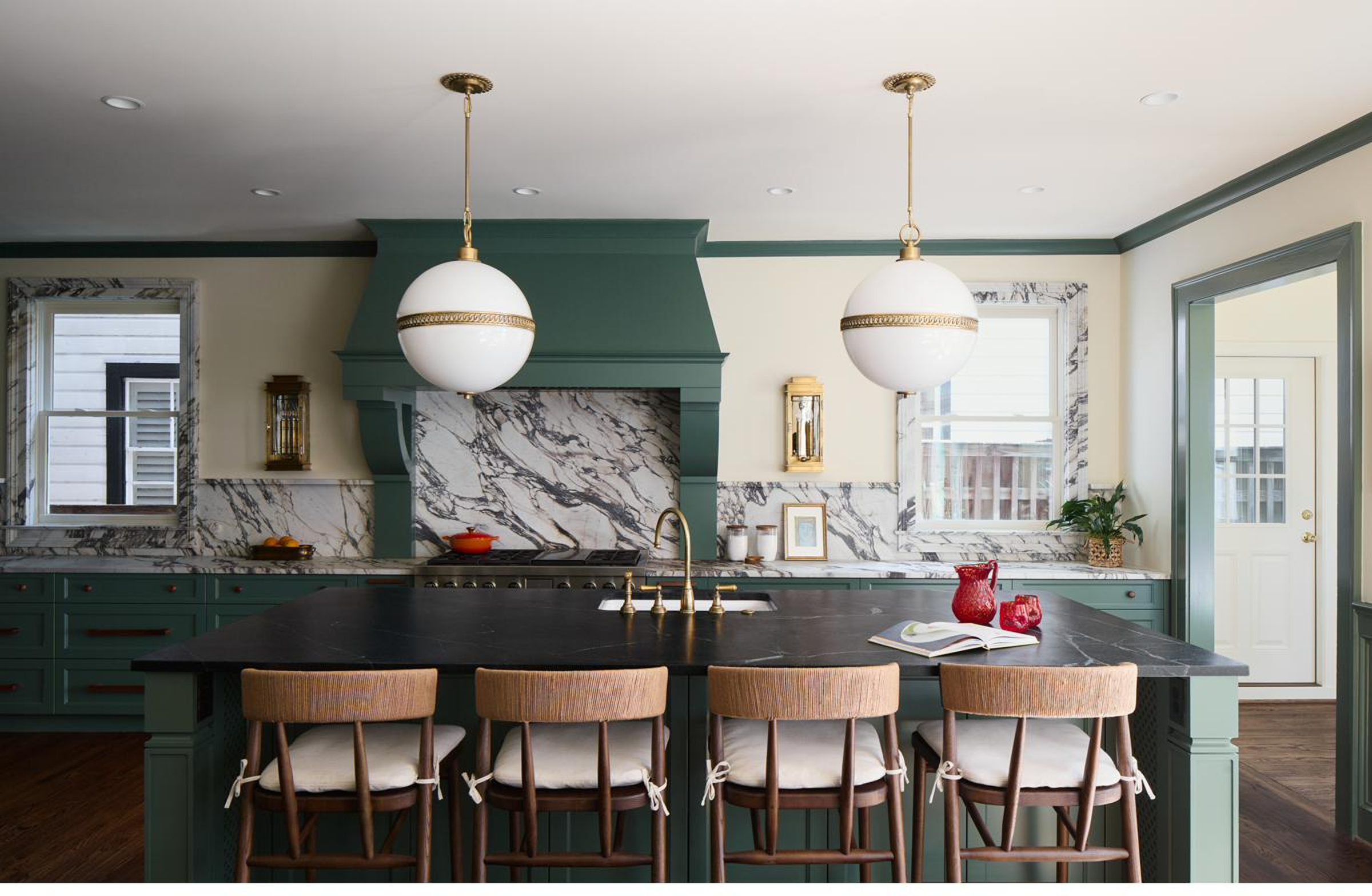 Sage green kitchen with marble slab backsplash and brass globe pendants